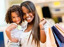Photo of woman holding shopping bags and child, both smiling at camera