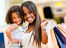 Photo of woman holding shopping bags and child, both smiling at camera