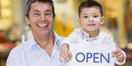 Photo of man next to child holding 'Open' sign