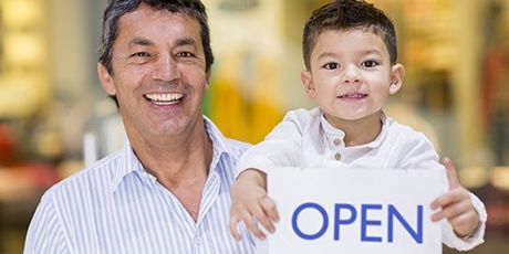 Photo of man next to child holding 'Open' sign